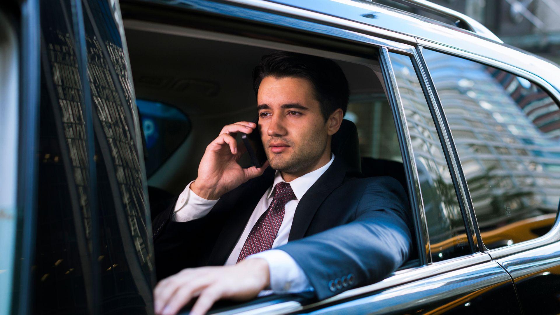 Businessman on a call in the back of a chauffeured black car hired by the hour